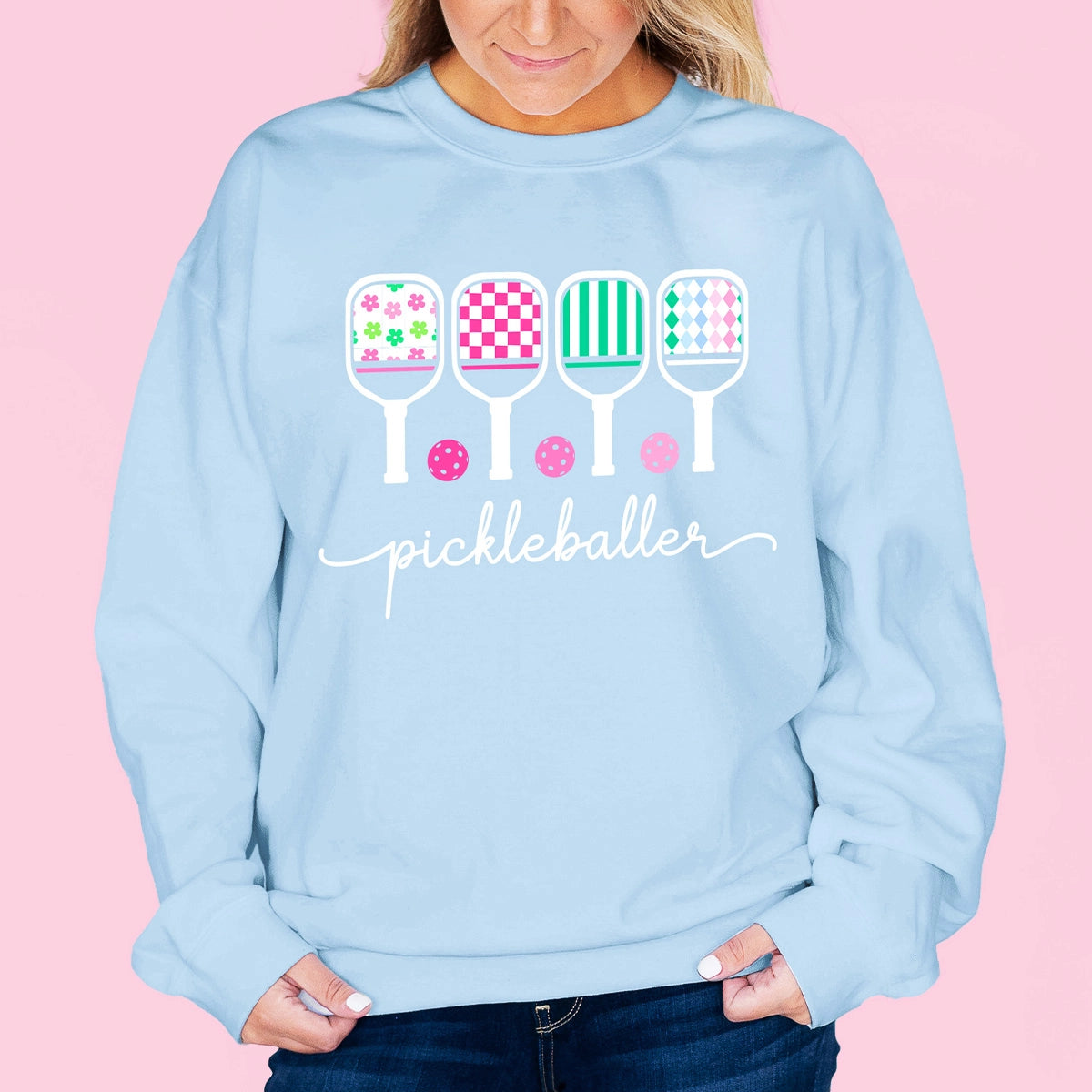 Woman wearing light blue sweatshirt with pickleball-themed design