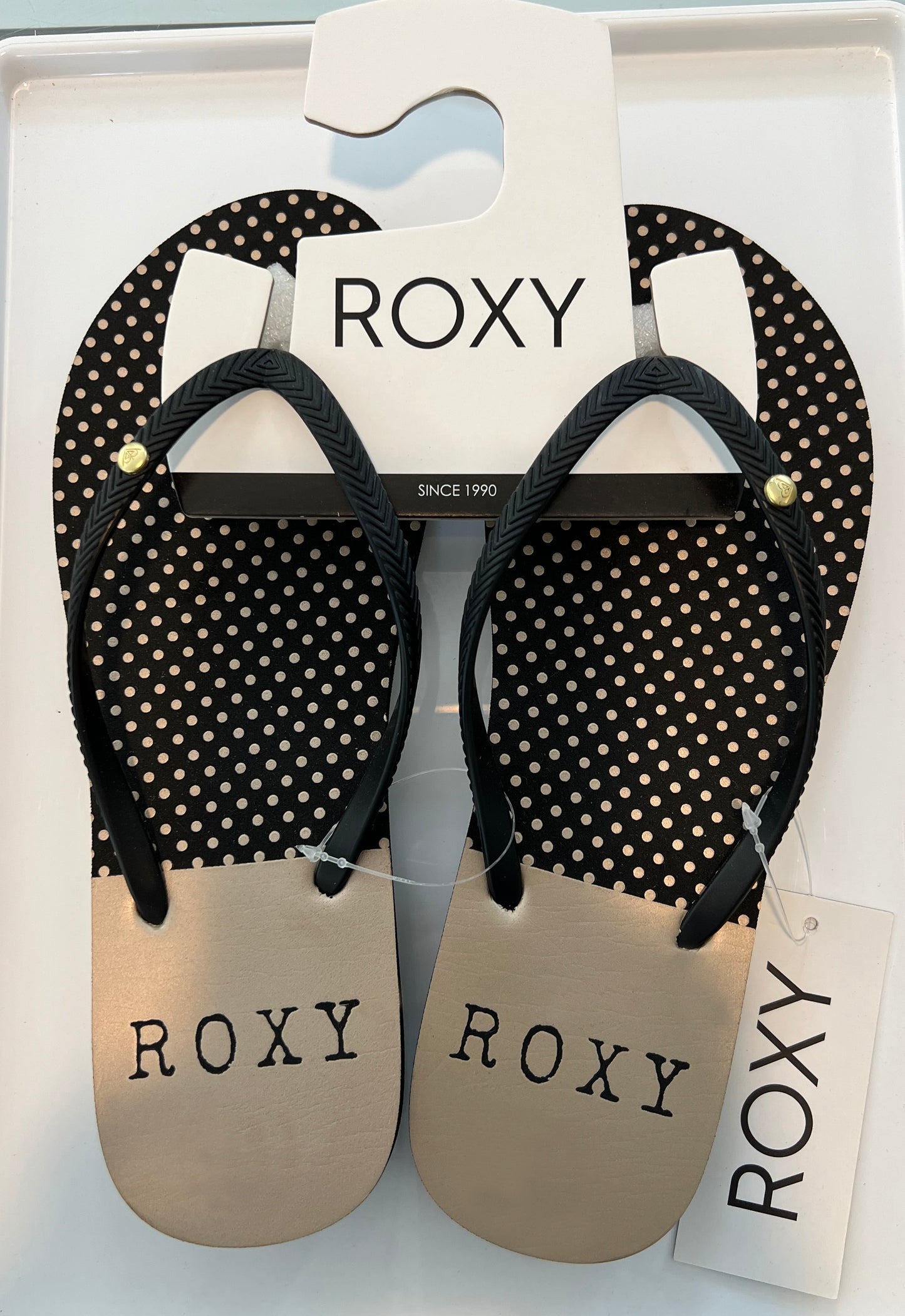 A pair of Roxy branded flip-flops in black color with a polka dot pattern on the straps