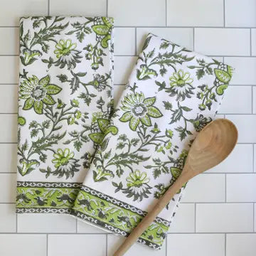 A green and white floral patterned kitchen towel is displayed on a surface with a wooden spoon beside it.