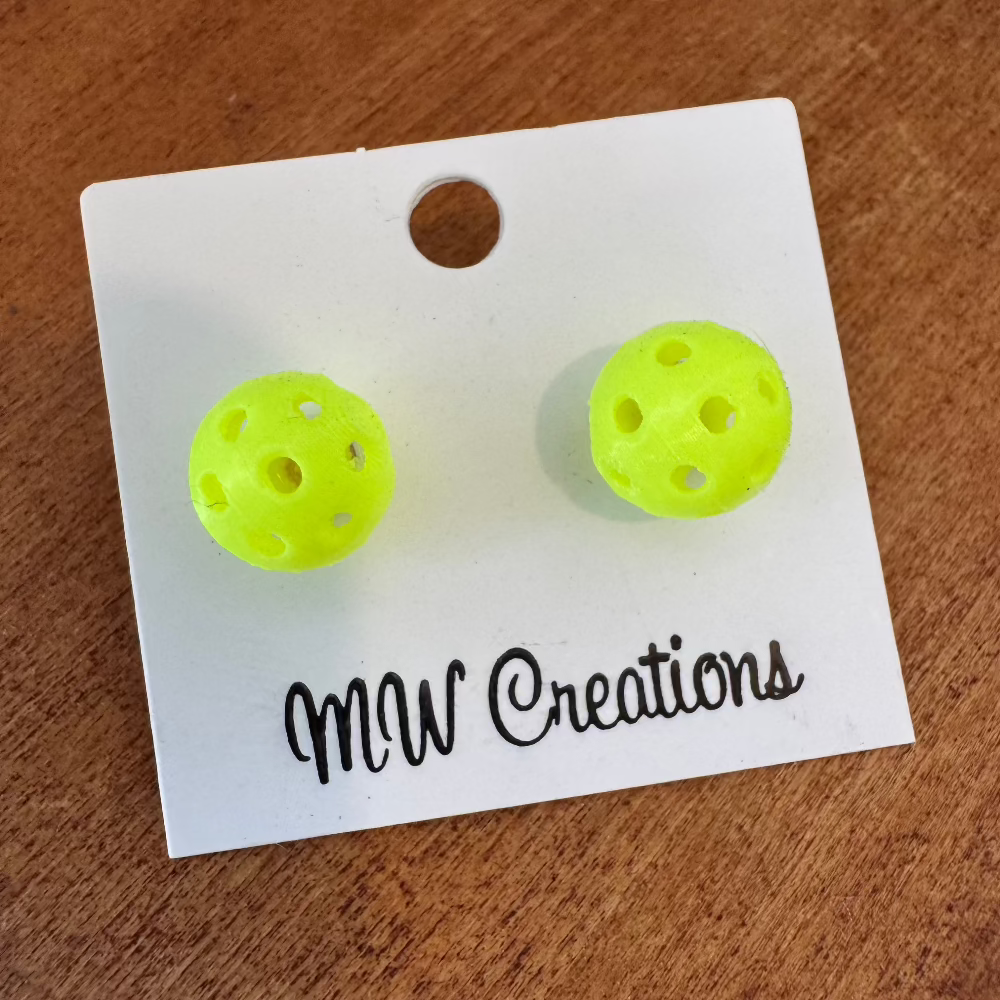 A pair of yellow pickleball earrings on a white display card with 'MW Creations' written at the bottom.