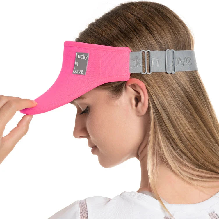 A pink visor with 'Lucky in Love' text on the front, worn by a woman.