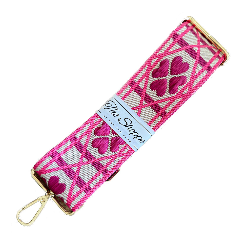 A pink and white heart design purse strap with gold hardwared clasps
