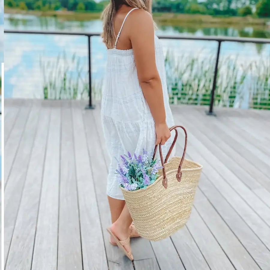 Model in white dress carrying woven straw bag with leather handle.