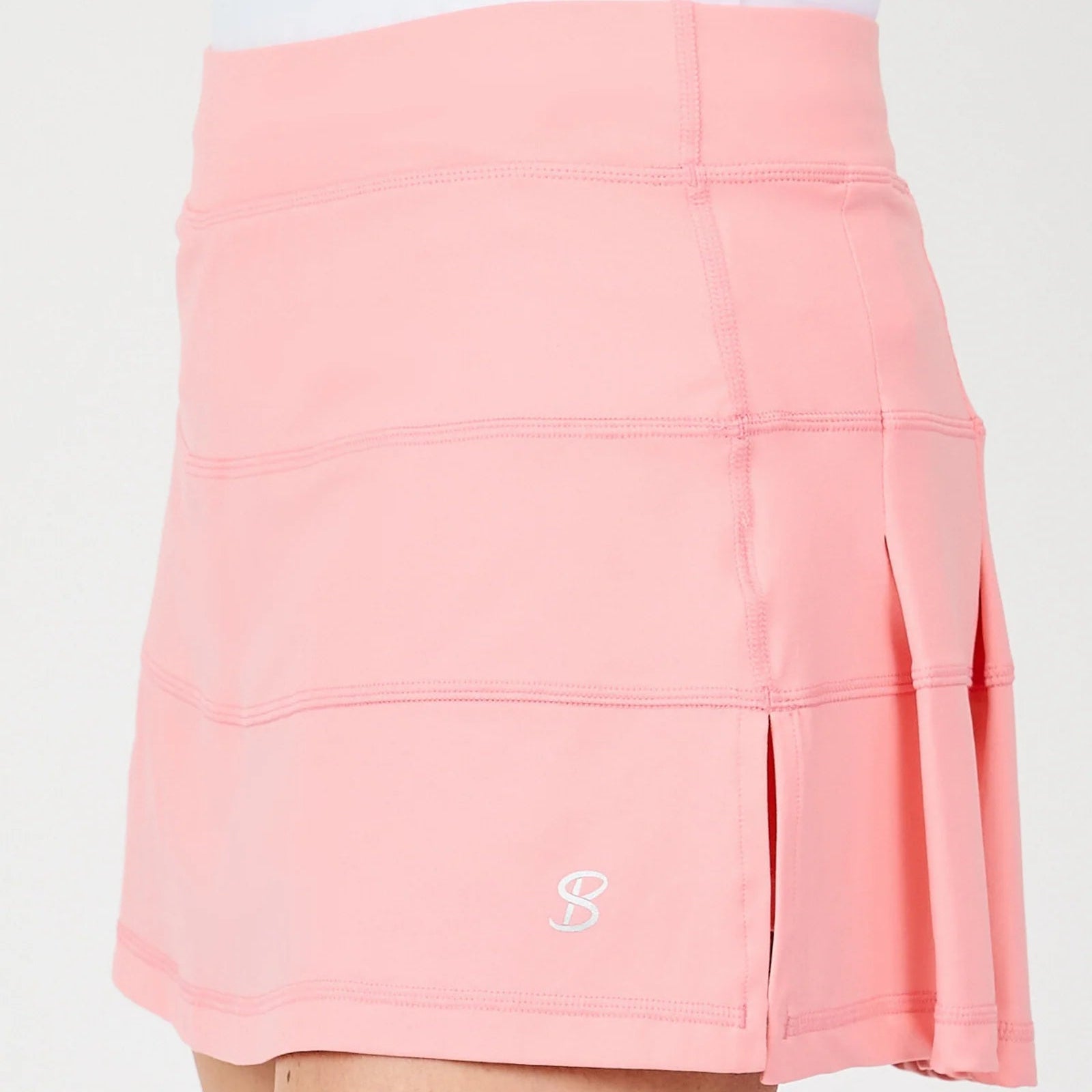 A close-up of a pink athletic skirt with horizontal seam panels and a small white Sofibella logo near the bottom left hem