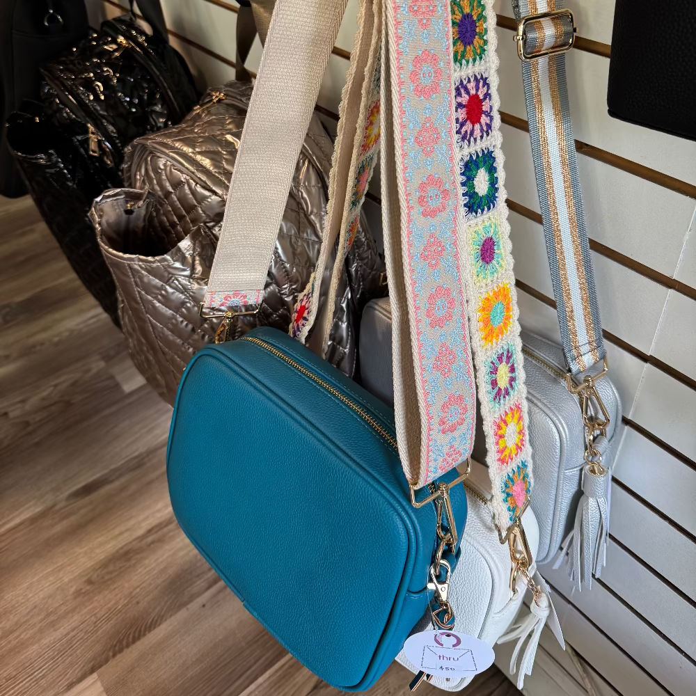 Aqua Blue bag with a colorful floral strap on a wooden floor.
