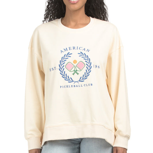 Woman wearing a cream sweatshirt with 'American Pickleball Club' logo on the front