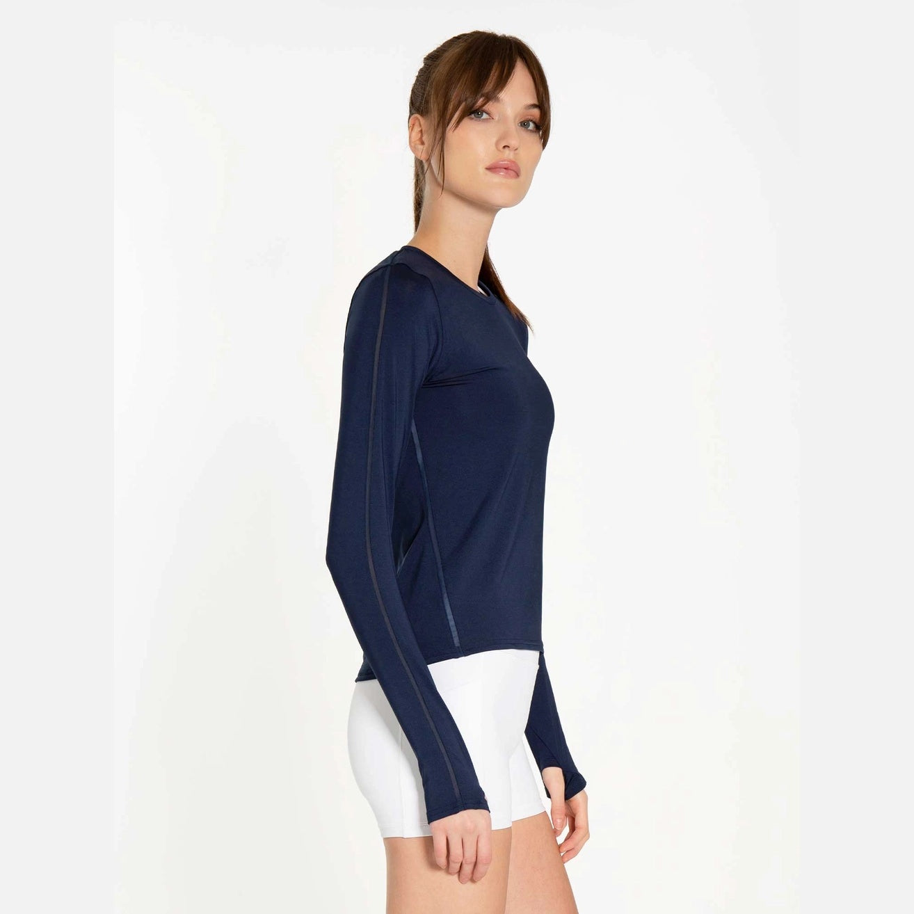 Side view of woman wearing a navy long-sleeve top and white shorts holding a pickleball paddle
