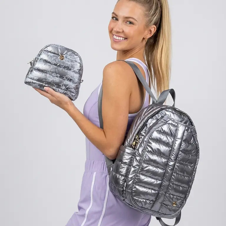 Model holding quilted nylon backpack with specialized paddle storage and a sporty aesthetic in shiny quilted steel gray silver and accessory bag
